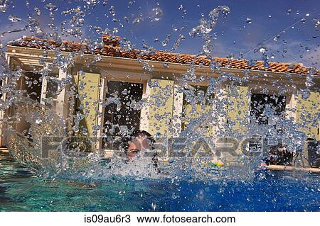 Stock Image - Teenage girl splashing in outdoor swimming pool. Fotosearch