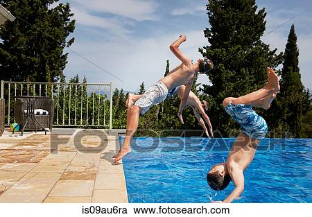 Stock Image - Three boys diving backward into apartment swimming pool. Fotosearch