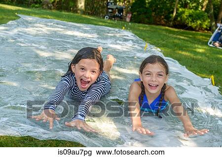 Two girls sliding on slip n slide water mat in garden View Large Photo Image Stock Image - Two girls sliding on slip n slide water mat in garden. Fotosearch
