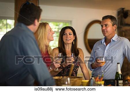 Stock Image - Two mature couples drinking white wine at dinner party. Fotosearch