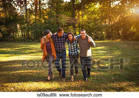 Stock Image - Two mature couples strolling in garden with arms around each other. Fotosearch