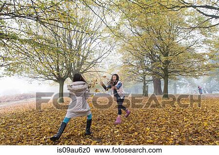 Two young girls playing, throwing leaves, in forest, autumn View Large Photo Image Stock Image - Two young girls playing, throwing leaves, in forest, autumn. Fotosearch