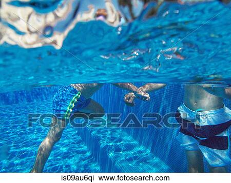 Stock Image - Underwater view of boys playing in swimming pool. Fotosearch