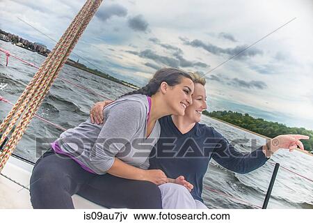 Women sitting side by side on sailboat looking away, pointing at view smiling View Large Photo Image Stock Photo - Women sitting side by side on sailboat looking away, pointing at view smiling. Fotosearch