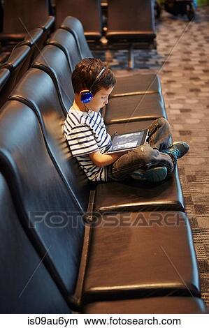Young boy sitting in airport waiting area, using digital tablet View Large Photo Image Picture - Young boy sitting in airport waiting area, using digital tablet. Fotosearch