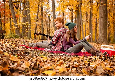 Stock Photo - Young couple back to back on picnic blanket in autumn forest. Fotosearch
