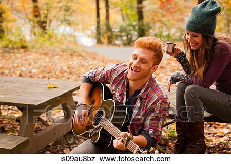 Stock Photo - Young couple playing guitar on picnic bench in autumn forest. Fotosearch