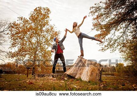 Young couple playing on tree stump in autumn park View Large Photo Image Stock Photograph - Young couple playing on tree stump in autumn park. Fotosearch