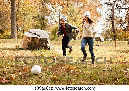 Stock Photo - Young couple running after soccer ball in autumn park. Fotosearch