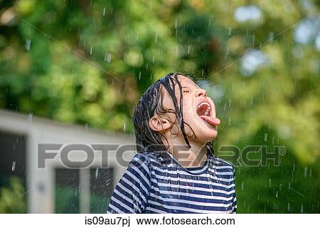 Stock Image - Young girl in garden, catching falling water in mouth. Fotosearch