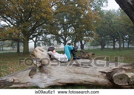 Stock Image - Young girl relaxing on tree stump in forest. Fotosearch