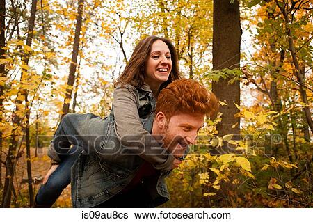 Young man giving girlfriend a piggy back through autumn forest View Large Photo Image Stock Photograph - Young man giving girlfriend a piggy back through autumn forest. Fotosearch