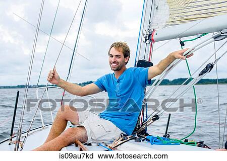 Young man sitting on sailboat looking at camera smiling View Large Photo Image Stock Image - Young man sitting on sailboat looking at camera smiling. Fotosearch