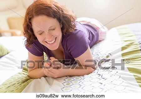Young woman lying on front on bed, eyes closed laughing View Large Photo Image Stock Photo - Young woman lying on front on bed, eyes closed laughing. Fotosearch