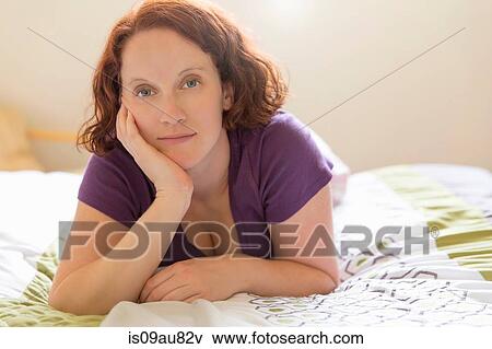 Young woman lying on front on bed, hand on chin looking at camera View Large Photo Image Stock Photo - Young woman lying on front on bed, hand on chin looking at camera. Fotosearch