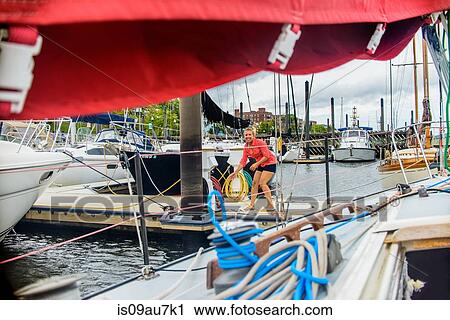 Stock Image - Young woman on marina pier mooring sailboat looking at camera smiling. Fotosearch