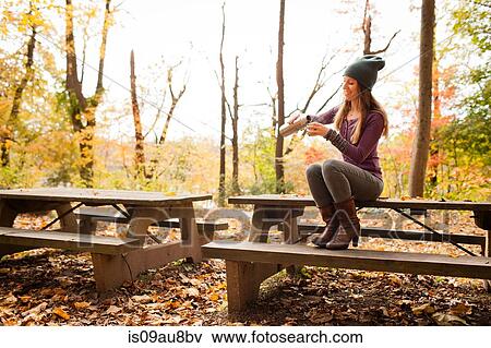 Young woman pouring drink on picnic bench in autumn forest View Large Photo Image Stock Photo - Young woman pouring drink on picnic bench in autumn forest. Fotosearch