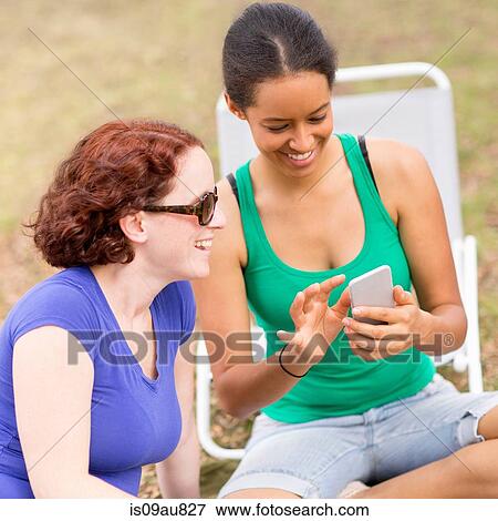 Young woman sitting crossed legs using smartphone, looking down smiling View Large Photo Image Stock Photo - Young woman sitting crossed legs using smartphone, looking down smiling. Fotosearch