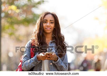 Young woman with long brown hair wearing denim jacket holding smartphone looking away smiling View Large Photo Image Stock Photo - Young woman with long brown hair wearing denim jacket holding smartphone looking away smiling. Fotosearch