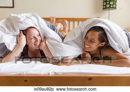 Young women lying on front in bed underneath quilt face to face smiling View Large Photo Image Stock Photography - Young women lying on front in bed underneath quilt face to face smiling. Fotosearch