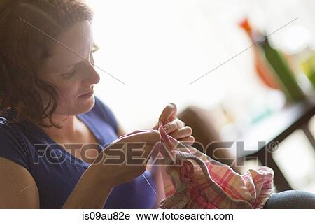 Stock Image - Young women repairing garment, looking down. Fotosearch