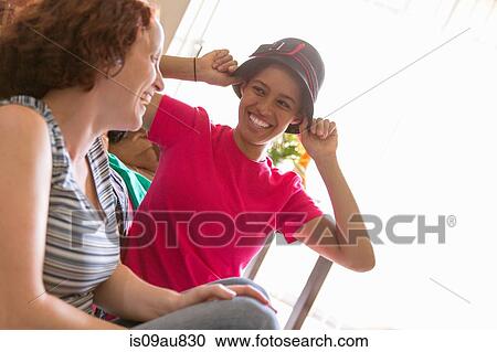 Young women trying on hat face to face smiling View Large Photo Image Stock Image - Young women trying on hat face to face smiling. Fotosearch