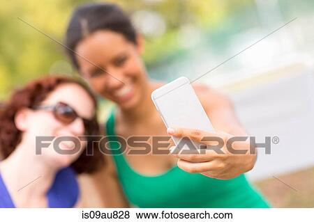 Young women using smartphone to take sefie smiling, focus on foreground View Large Photo Image Stock Photo - Young women using smartphone to take sefie smiling, focus on foreground. Fotosearch