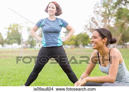 Young women wearing sports clothing in field stretching, looking away smiling View Large Photo Image Picture - Young women wearing sports clothing in field stretching, looking away smiling. Fotosearch