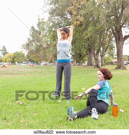 Stock Image - Young women wearing sports clothing on grass stretching. Fotosearch
