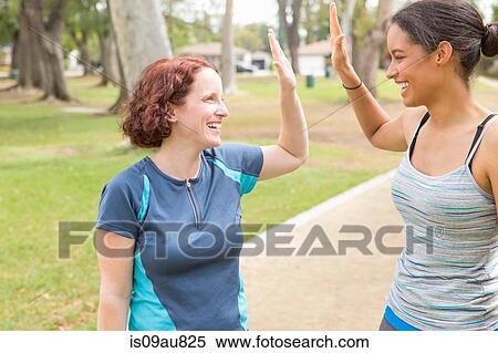 Young women wearing sports clothing face to face smiling doing high five View Large Photo Image Stock Photography - Young women wearing sports clothing face to face smiling doing high five. Fotosearch