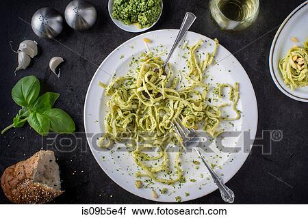 Stock Image - A devoured plate of pesto pasta with ingredients surrounding plate and a glass of white wine, overhead view. Fotosearch
