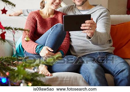 Picture - Adult couple sitting on sofa reading digital tablet at xmas. Fotosearch