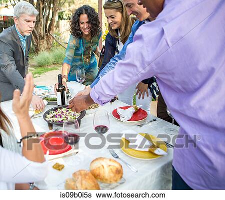 Adult friends helping themselves to food and drink at garden party table View Large Photo Image Stock Photograph - Adult friends helping themselves to food and drink at garden party table. Fotosearch