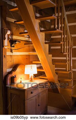 Stock Photography - Antique wooden cabinet below uneven wooden stairs in Canadiana cottage-style log home, Quebec, Canada. Fotosearch