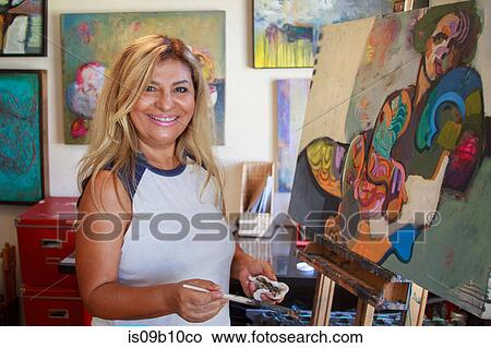 Artist painting artwork on canvas, looking at camera smiling View Large Photo Image Picture - Artist painting artwork on canvas, looking at camera smiling. Fotosearch