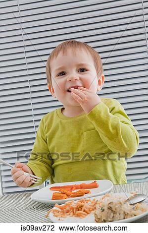 Baby boy feeding himself at dining table View Large Photo Image Stock Image - Baby boy feeding himself at dining table. Fotosearch
