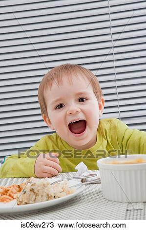 Baby boy feeding himself at dining table View Large Photo Image Stock Image - Baby boy feeding himself at dining table. Fotosearch