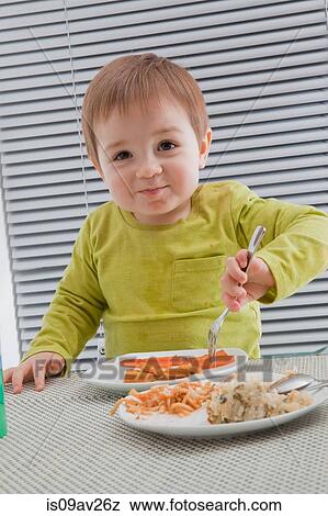 Stock Photo - Baby boy feeding himself at dining table. Fotosearch