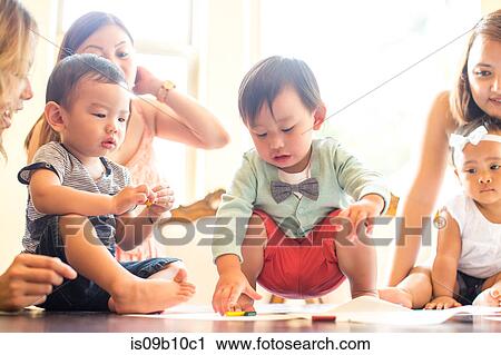 Stock Image - Baby boy picking up crayon on dining room table. Fotosearch