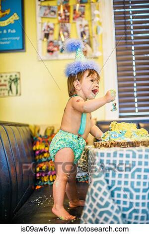 Baby boy wearing party hat messying first birthday cake at table View Large Photo Image Stock Photography - Baby boy wearing party hat messying first birthday cake at table. Fotosearch