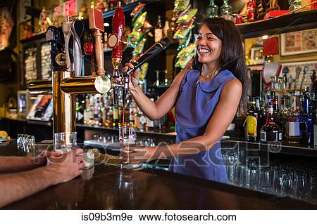 Stock Image - Barmaid serving beer from pump in public house. Fotosearch