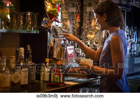 Stock Image - Barmaid using cash register in public house. Fotosearch