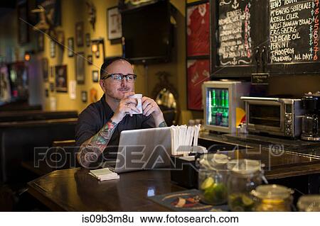 Stock Photograph - Barman having a coffee break at public house table. Fotosearch