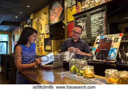 Stock Image - Barman laughing with female customer at public house counter. Fotosearch