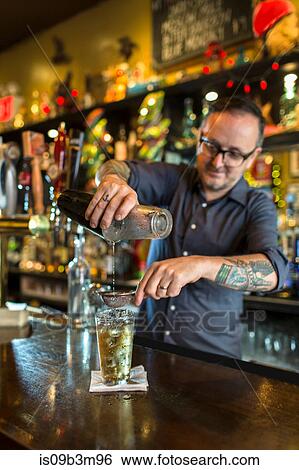 Barman pouring cocktail into glass at public house counter View Large Photo Image Stock Photograph - Barman pouring cocktail into glass at public house counter. Fotosearch