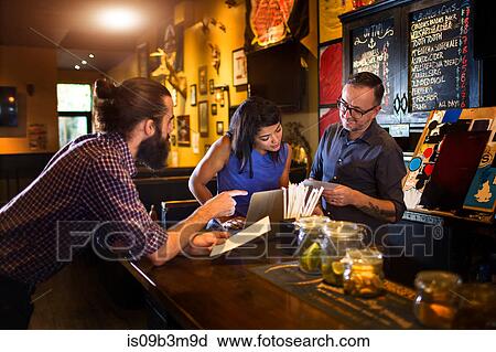 Barman reading menu with young couple at public house counter View Large Photo Image Stock Image - Barman reading menu with young couple at public house counter. Fotosearch