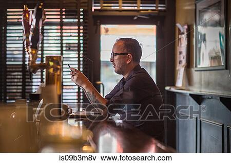 Barman reading smartphone texts at public house counter View Large Photo Image Stock Photo - Barman reading smartphone texts at public house counter. Fotosearch