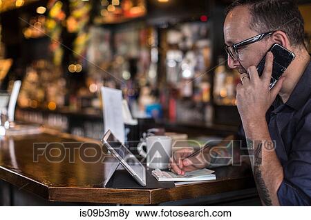 Barman talking on smartphone at public house counter View Large Photo Image Stock Photo - Barman talking on smartphone at public house counter. Fotosearch