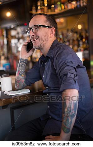 Stock Photo - Barman talking on smartphone at public house counter. Fotosearch