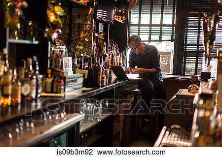 Barman typing on laptop at public house counter View Large Photo Image Stock Image - Barman typing on laptop at public house counter. Fotosearch